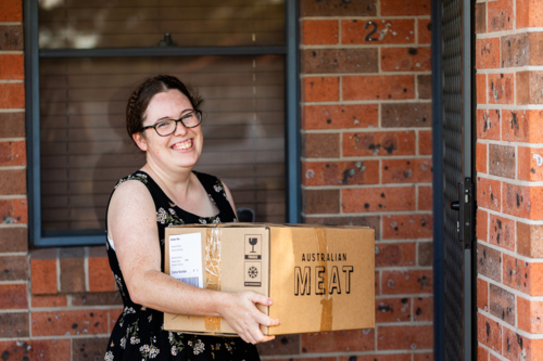 Woman by front door of home collecting box from online meat order delivery - Australian Stock Image