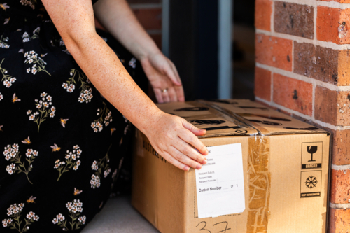 Woman by front door of home collecting box from online order delivery   - Australian Stock Image