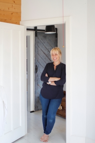 Woman casually leaning against doorway in white walled home - Australian Stock Image