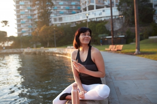 Woman checking phone by harbour at sunrise - Australian Stock Image