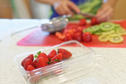 Woman cutting up strawberries and kiwi fruit on a cutting board - Australian Stock Image
