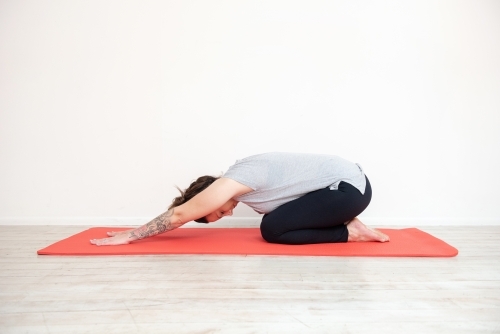 woman doing childs pose yoga on red mat in studio