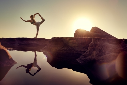Woman doing yoga by the ocean with sun flare - Australian Stock Image
