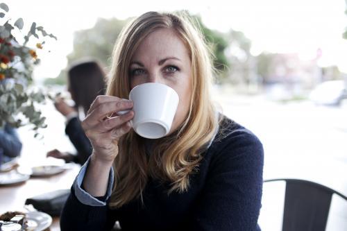 Woman drinking coffee from a mug outside cafe - Australian Stock Image