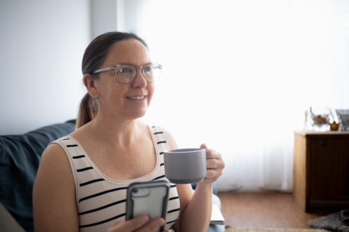 Woman drinking coffee on couch looking off to the side - Australian Stock Image