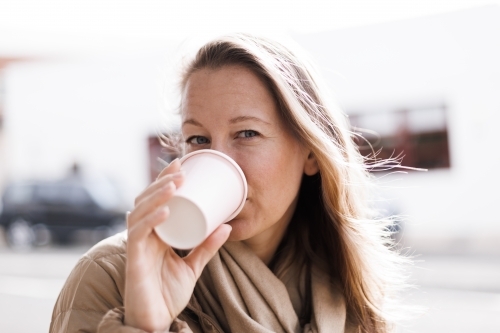 Woman drinking from a coffee cup with urban background - Australian Stock Image