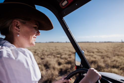 Woman driving a farm vehicle in a dry grassy field on a sunny day - Australian Stock Image