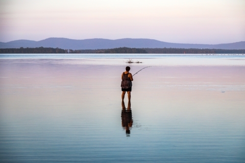 Woman fishing in lake with reflection in water - Australian Stock Image
