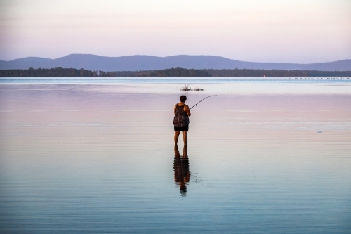 Woman fishing in lake with reflection in water