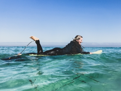 Woman floating on surfboard in wetsuit with seaweed boa - Australian Stock Image