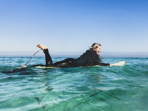 Woman floating on surfboard in wetsuit with seaweed boa