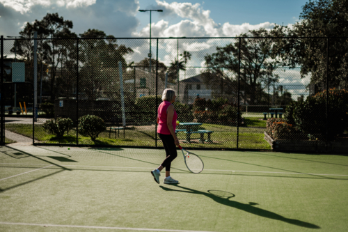 Woman has fun playing tennis outdoors on a green court under bright sunlight - Australian Stock Image