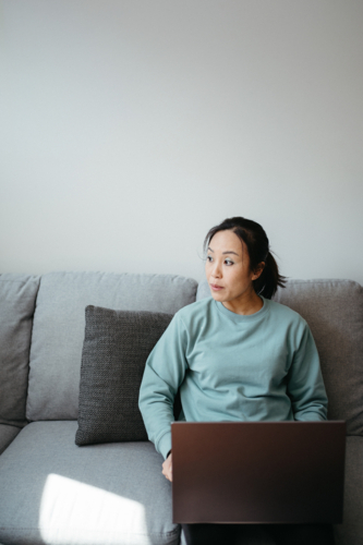 Woman holding a laptop while sitting on the sofa - Australian Stock Image