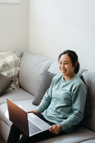 Woman holding a laptop while sitting on the sofa - Australian Stock Image