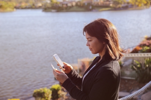 Woman holding credit card and mobile by the lake, online shopping, internet banking concept - Australian Stock Image