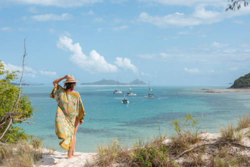 woman holding hat, wearing kimono looking out over calm bay of ocean with islands in background - Australian Stock Image