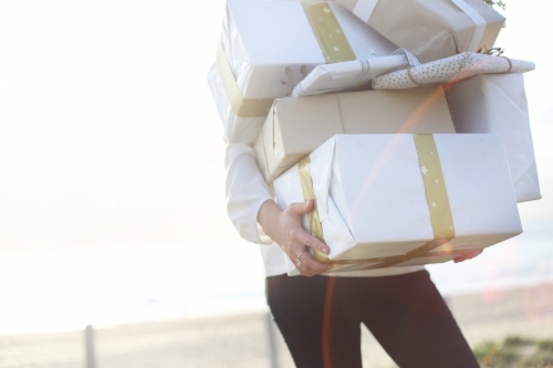 Woman holding presents with beach in background - Australian Stock Image