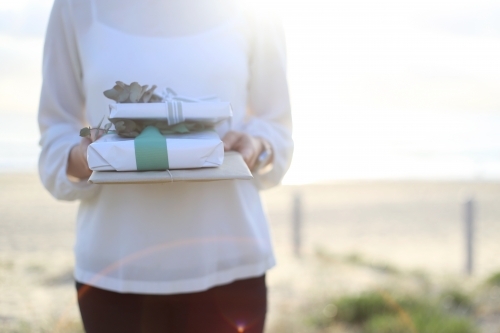 Woman holding presents with beach in background - Australian Stock Image