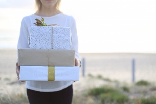 Woman holding presents with beach in background - Australian Stock Image