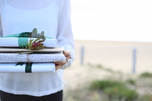 Woman holding presents with beach in background - Australian Stock Image