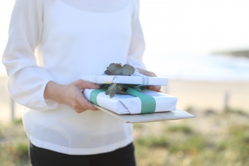 Woman holding presents with beach in background - Australian Stock Image
