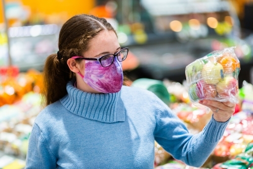 Woman holding up pack of fresh fruit covered in plastic, grocery shopping during covid - Australian Stock Image