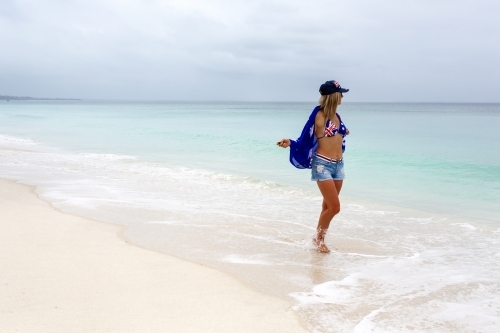 Woman holidaying on a beach in Australia. She has a flag draped over her shoulder - Australian Stock Image