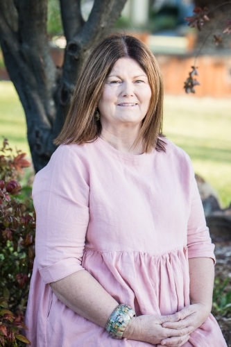 Woman in 50s sitting in garden smiling - Australian Stock Image