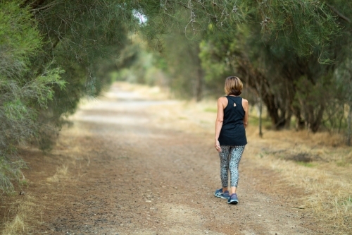 woman in activewear walking away down  country lane - Australian Stock Image