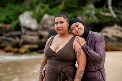 Woman in burkini resting her head on her friends shoulder on the beach - Australian Stock Image