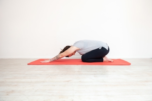 woman in child's pose doing yoga on mat in studio