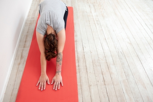 woman in child's pose on red mat in studio - Australian Stock Image
