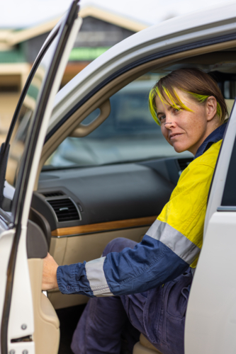 woman in hi-vis workwear looking out of the passenger door in a 4WD wagon - Australian Stock Image