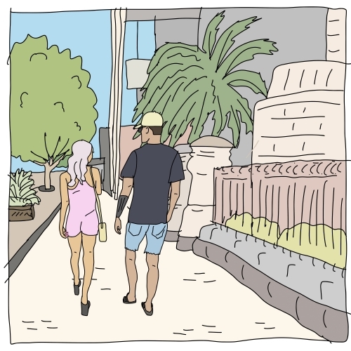 Woman in pink jumpsuit, man in black t-shirt and denim shorts walking on footpath past buildings - Australian Stock Image