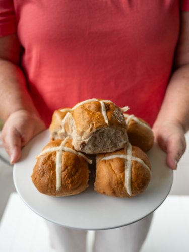 Woman in pink shirt holding white plate of hot cross buns - Australian Stock Image