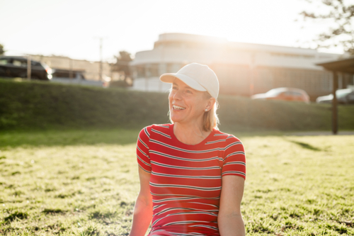 Woman in stripe shirt, sitting in a grassy park under the warm afternoon sun, smiling and relaxed. - Australian Stock Image