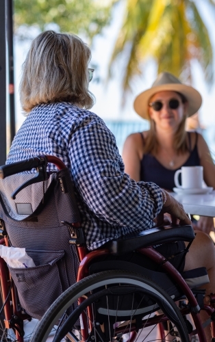 woman in wheelchair having cuppa with  younger woman near palm trees