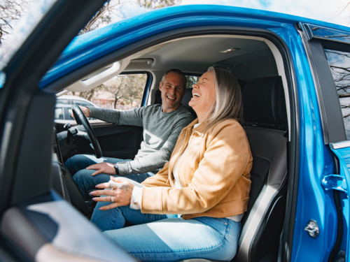 Woman inside blue car laughing with man seated behind the wheel - Australian Stock Image