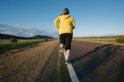Woman jogging away on a remote country road - Australian Stock Image