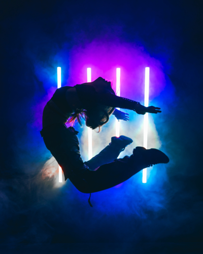 Woman Jumping in Front of Purple and Blue Neon Lights - Australian Stock Image