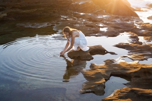 Woman kneeling beside rockpool with golden light and ripples
