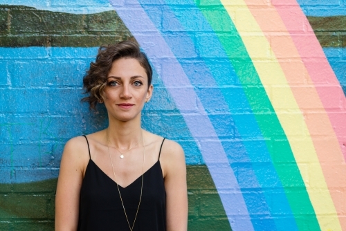 woman leaning against brick wall with rainbow - Australian Stock Image
