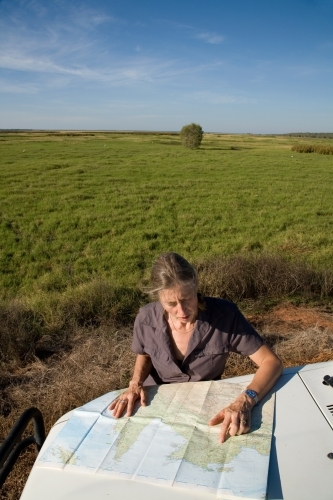 Woman leaning of the bonnet of her car in rural area, reading a map - Australian Stock Image