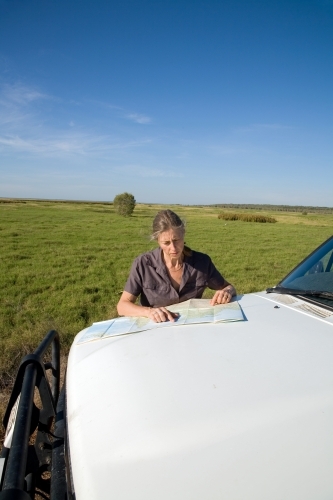 Woman leaning of the bonnet of her car in rural area, reading a map