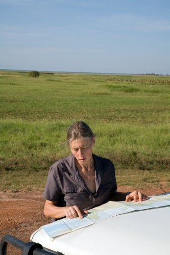 Woman leaning of the bonnet of her car in rural area, reading a map