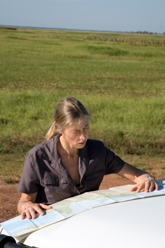 Woman leaning of the bonnet of her car in rural area, reading a map - Australian Stock Image