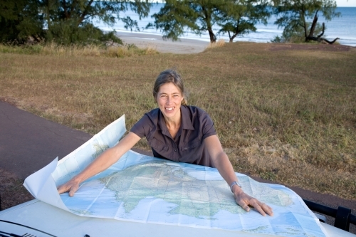 Woman leaning on bonnet of car with map, smiling at the camera - Australian Stock Image