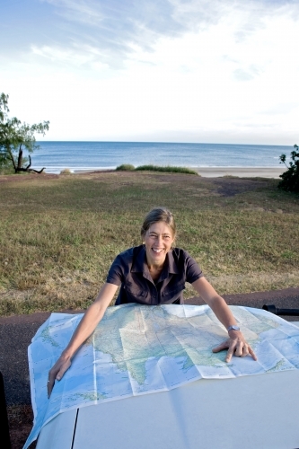 Woman leaning on bonnet of car with map, smiling - Australian Stock Image