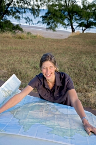 Woman leaning on bonnet of car with map, smiling - Australian Stock Image