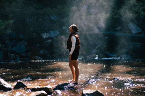 Woman looking up at waterfall in the mist - Australian Stock Image